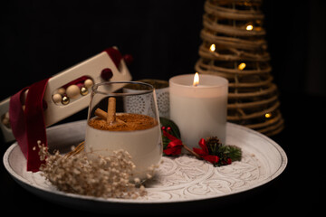 Rompope with cinnamon sticks, christmas decoration and burning candle celebrating christmas