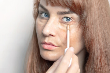 Girl Woman applies applicator concealer under her eyes. Close up photo