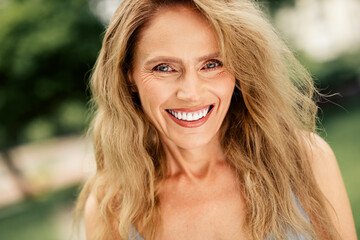 Fototapeta premium Charming middle-aged woman smiling warmly outdoors with natural surroundings on a sunny day, radiating happiness