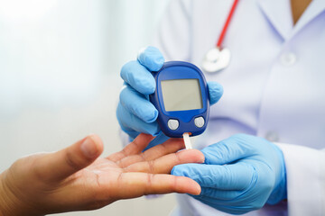 Asian doctor using digital glucose meter for check sample blood sugar level to treatment diabetes.