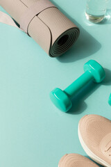 Sport or workout concept flat lay with blue dumbbells, bottle of water, sneakers, yoga mat on the blue teal background. Copy space