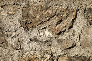 Close-up detail of a rough stone wall featuring natural rocks set in concrete mortar, emphasizing texture and material contrast.