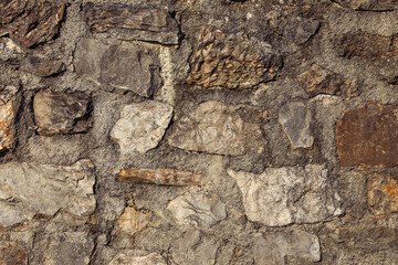Natural stones are embedded in concrete mortar, creating a rough textured close-up of a stone wall with detailed surfaces.