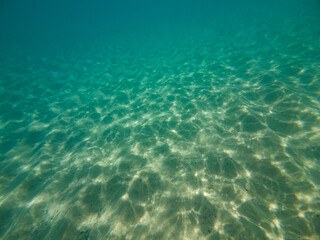 Clear turquoise water reveals a sandy ocean floor with gentle light reflections.
