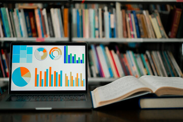 A laptop screen displaying a graph and a book placed on the table in the library, representing a business concept.	