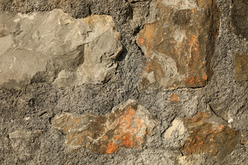 This is a close-up photo of a rough textured stone wall made of natural rocks embedded in concrete mortar. The image shows detailed textures of concrete and stone.