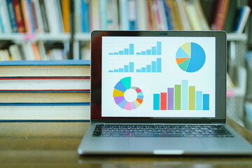 A laptop screen displaying a graph and a book placed on the table in the library, representing a business concept.	