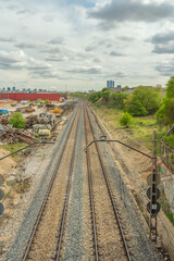 Obraz premium Straight section of commuter rail track with gray ballast and concrete sleepers, flanked by a safety fence and overhead power lines