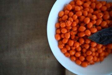  A close-up shot of a white bowl filled with bright orange sea buckthorn berries and a basil leaf, symbolizing warmth, health, and natural vitamins.