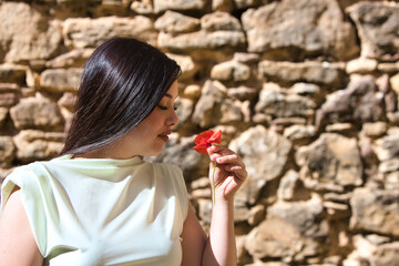 A beautiful Spanish teenager with long dark hair picks up a delicate, beautiful red poppy, smells...