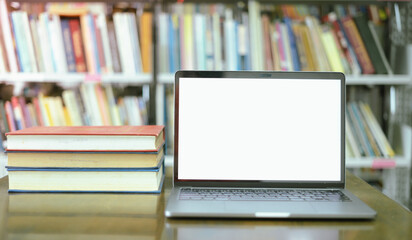 There is a laptop with a white screen and a book placed on the table in the library.