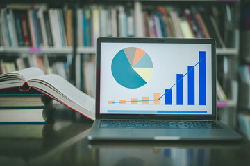 A laptop screen displaying a graph and a book placed on the table in the library, representing a business concept.	