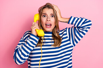 Surprised casual young woman holding a yellow phone receiver against a pink background, expressing shock and worry