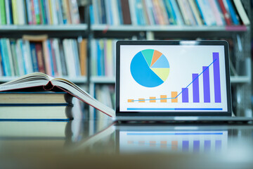 A laptop screen displaying a graph and a book placed on the table in the library, representing a business concept.	