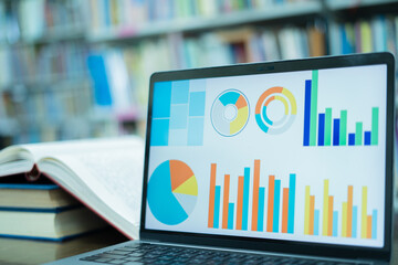 A laptop screen displaying a graph and a book placed on the table in the library, representing a business concept.	