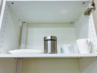 An organized kitchen cabinet has a sturdy shelf filled with neatly arranged plates, various cups,...