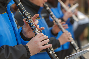 Musicians dressed in matching blue jackets perform with clarinets at a lively outdoor event during the afternoon.