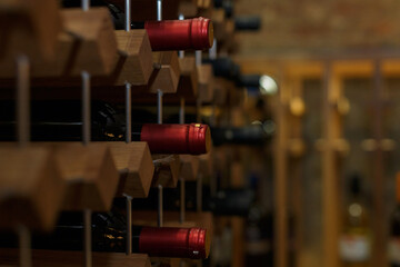 A collection of wine bottles with red caps arranged on wooden shelving in a rustic wine cellar...