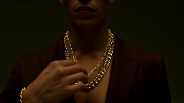 Man wearing a thick gold chain and a dark suit, looking directly at the camera with a serious expression