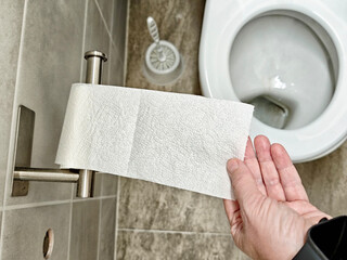 Person reaching for a roll of toilet paper in a clean bathroom setting