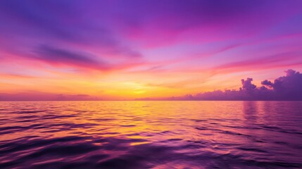Fototapeta premium A stunning sunset over calm waters, showcasing vibrant hues of purple, orange, and pink in the sky, reflecting beautifully on the surface of the ocean.