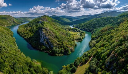 Fototapeta premium Serpentine river meanders through lush green hills and valleys under a partly cloudy sky
