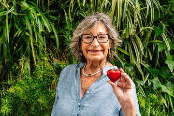 Senior woman holding red heart smiling for love and care