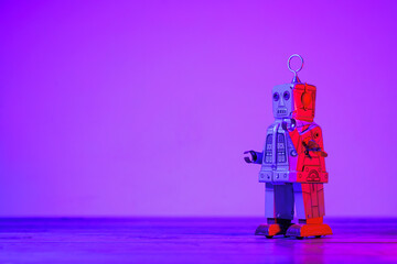 Retro tin wind-up robot toy standing on a wooden surface with a vibrant purple and red neon light background, creating a futuristic and nostalgic atmosphere
