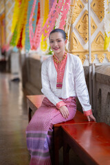 Woman in traditional attire sits on bench, surrounded by colorful decorations and intricate patterns, exuding cultural elegance