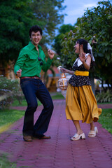 joyful couple dancing brick path park. man is wearing green shirt and jeans while woman is yellow
