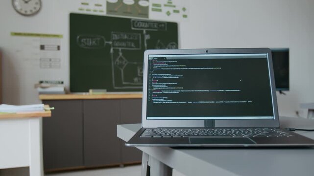 No people shot of IT classroom with chalkboard with flowchart illustrating counting algorithm and laptop displaying code