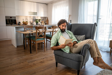 Man relaxing at home, enjoying book on armchair