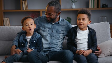 Happy African American family portrait dad with children looking at camera at home smiling cuddle...