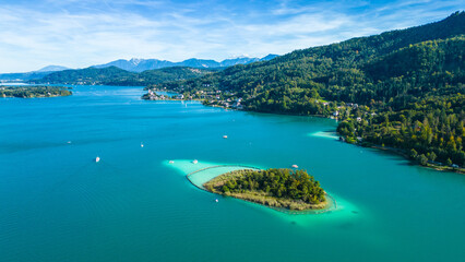 Aerial view of Portschach am Worthersee, Austria, with turquoise lake waters, boats, piers and alpine scenery. Popular summer holiday destination for relaxation, wellness and tourism