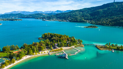Aerial view of Portschach am Worthersee, Austria, with turquoise lake waters, boats, piers and alpine scenery. Popular summer holiday destination for relaxation, wellness and tourism
