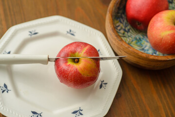 A knife that cut a red apple on a white plate