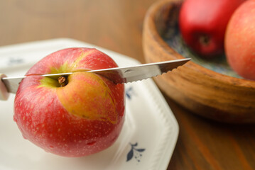 A knife that cut a red apple on a white plate