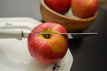 A knife that cut a red apple on a white plate