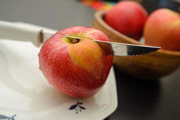 A knife that cut a red apple on a white plate