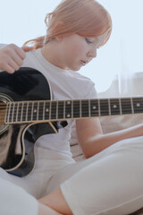 Fototapeta premium A teenage girl plays guitar in a bright living room, captured in an authentic moment of musical passion. Real photography showcasing genuine youth creativity and emotion