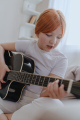 A teenage girl plays guitar in a bright living room, captured in an authentic moment of musical passion. Real photography showcasing genuine youth creativity and emotion