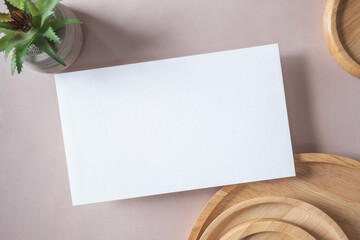 Empty white blank greeting or invitation card, cactus, wooden plate on beige background. Mock up presentation.