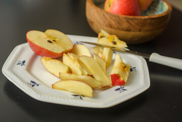 A knife that cut a red apple on a white plate