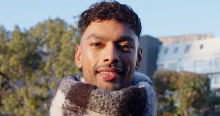 Asian man wearing thick knit scarf standing outdoors with trees, building blinking, greeting viewer - Powered by Adobe