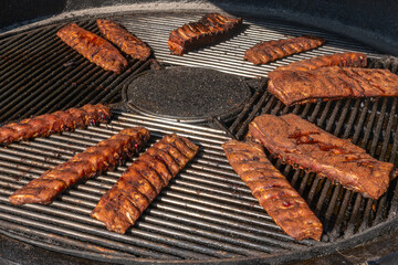 Grilled ribs cooking on round barbecue grill. Delicious barbecue pork ribs with crispy dry rub seasoning placed on circular grill ready for serving.