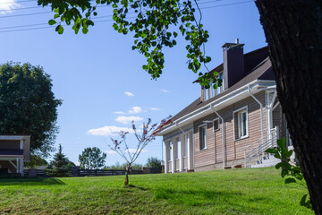 Residential house with porch lawn and wooden structures under clear blue sky. Well maintained countryside home with porch carport and wooden annex ideal for real estate architecture lifestyle.