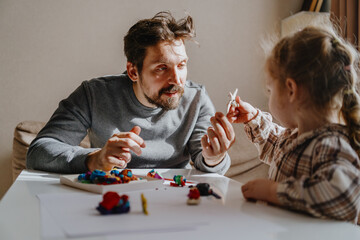 A 3-year-old girl and her father play with modeling clay in a sunny living room. Unfiltered,...