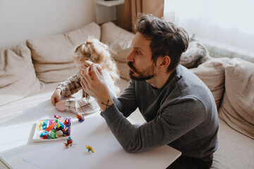 A 3-year-old girl and her father play with modeling clay in a sunny living room. Unfiltered,...