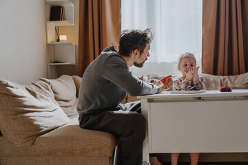A 3-year-old girl and her father play with modeling clay in a sunny living room. Unfiltered,...