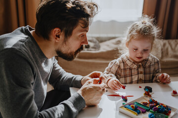 A 3-year-old girl and her father play with modeling clay in a sunny living room. Unfiltered,...